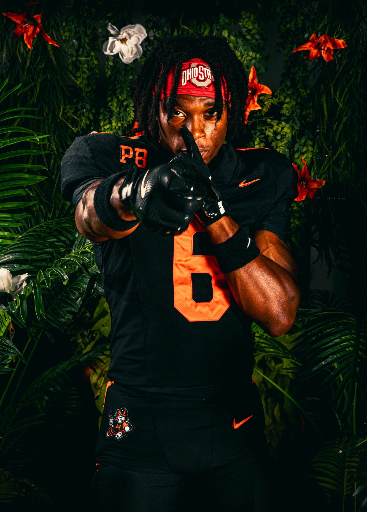 Athlete portrait in a black and orange football uniform against foliage.