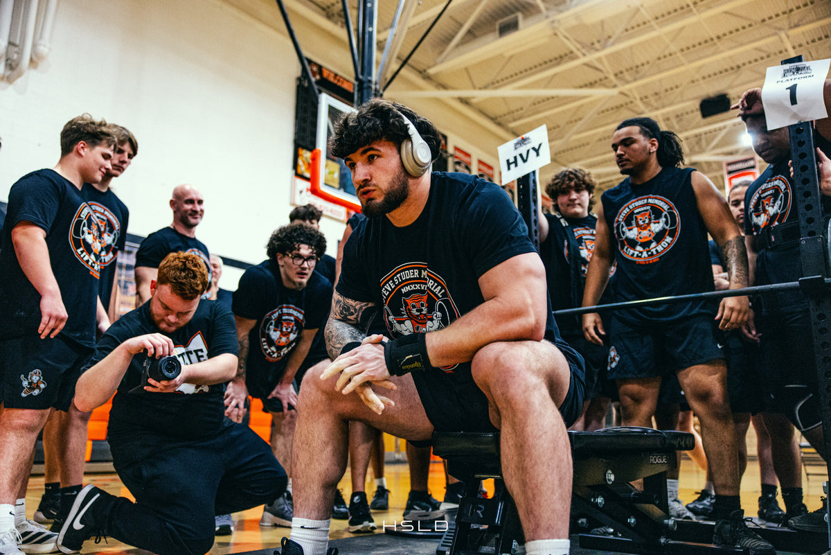 Athlete preparing for a lift as teammates and a photographer look on.