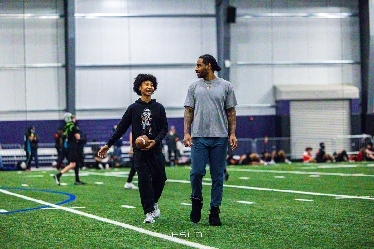 Two people walking together with a football on an indoor turf field.