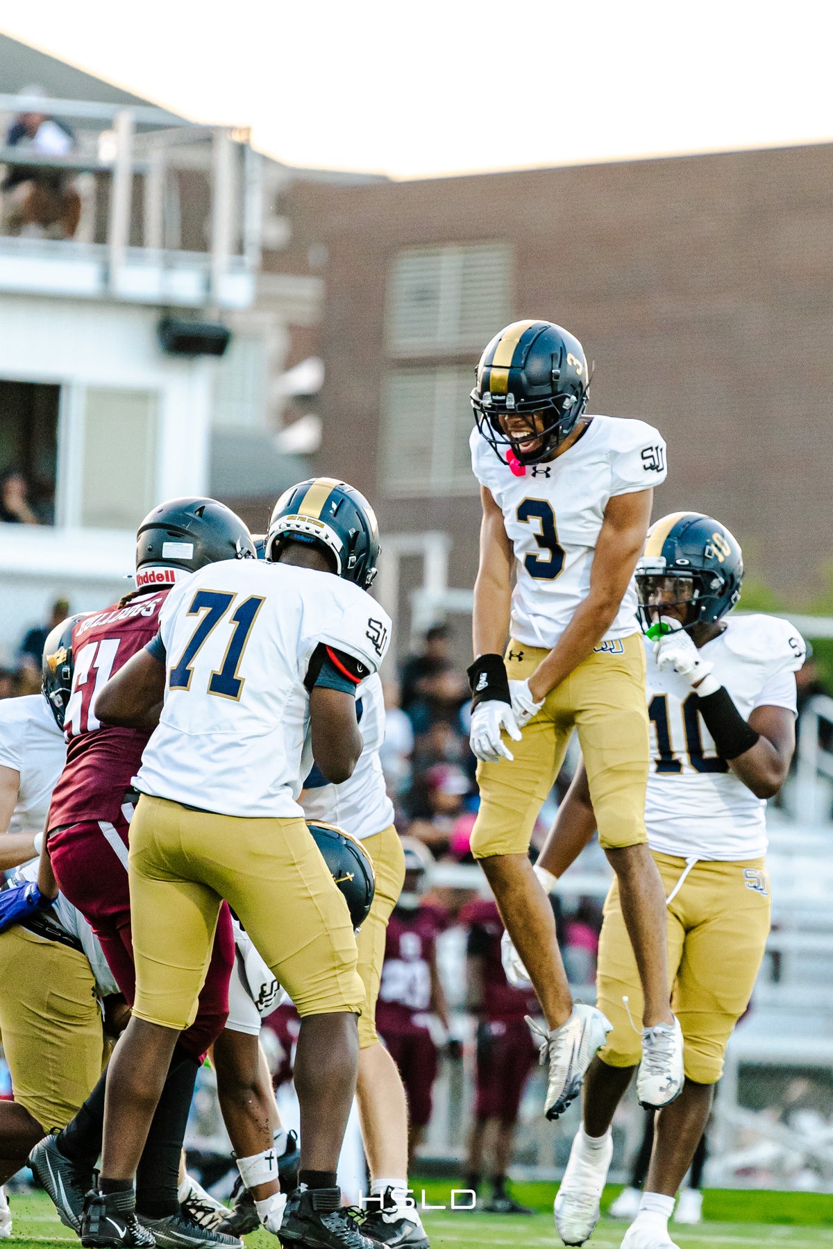 Football players in white and gold uniforms celebrating together.